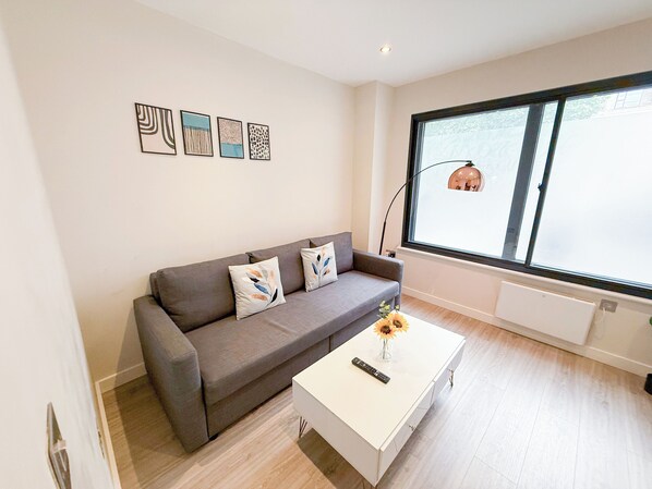 Una sala de estar moderna con un sofá gris, una mesa de centro blanca y un ventanal con vistas al exterior.