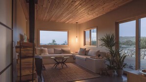 Ein modernes Wohnzimmer mit Holzboden, großen Fenstern, einer Sofagarnitur, einem Couchtisch und einer Topfpflanze.