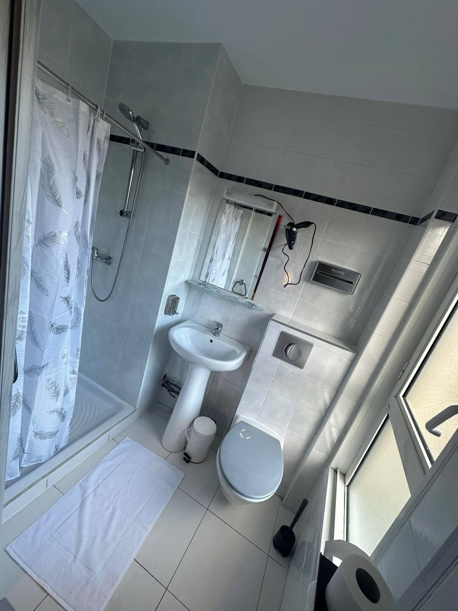 A compact bathroom with a shower, sink, toilet, and a window.