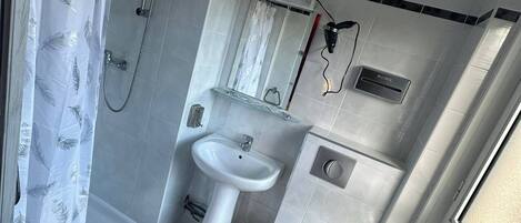 A compact bathroom with a shower, sink, toilet, and a window.