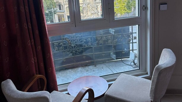 Ein Zimmer mit großem Fenster, zwei Stühlen, einem kleinen Tisch und Blick auf Gebäude.