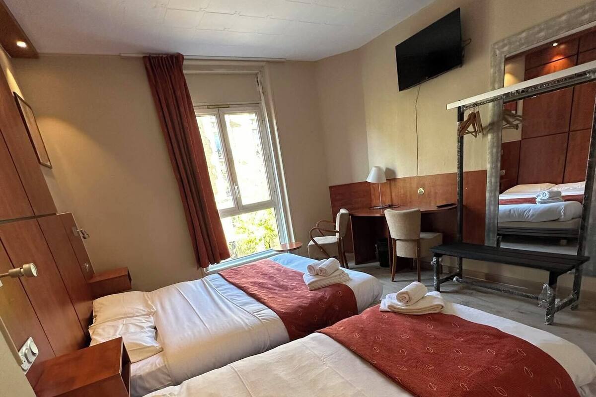 Une chambre d’hôtel avec deux lits, un bureau, une chaise, une télévision et un grand miroir.
