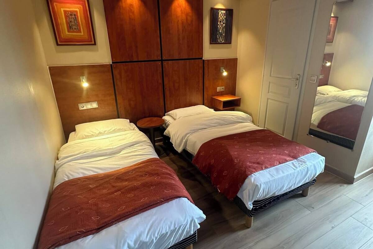 Une chambre d’hôtel avec deux lits, des têtes de lit en bois et des lampes fixées au mur.