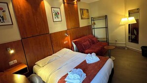 Ein Hotelzimmer mit Holz-Kopfteil, einem Bett mit weißer und roter Bettwäsche, einem Schreibtisch mit Stuhl und einem Nachttisch.