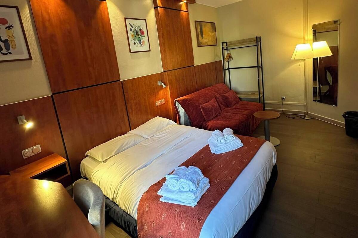 Une chambre d’hôtel avec une tête de lit en bois, un lit avec une literie blanche et rouge, un bureau avec une chaise et une table de chevet.
