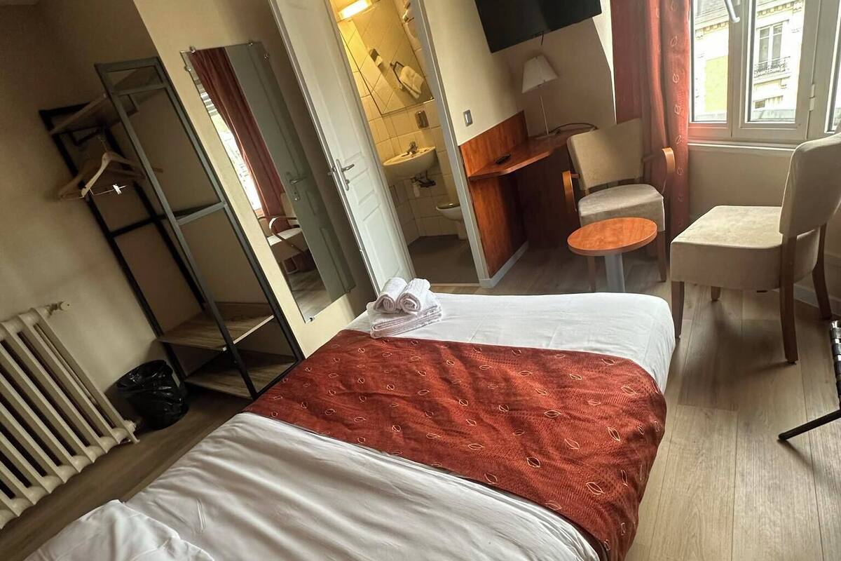 Une chambre d’hôtel avec deux lits, un coin salon avec une table et des chaises, un téléviseur fixé au mur et une fenêtre avec des rideaux.