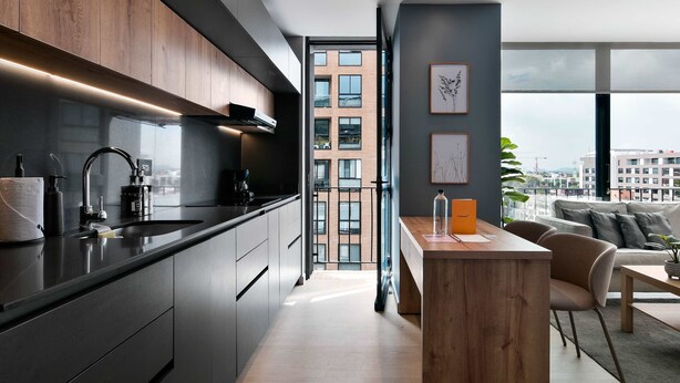 A modern kitchen with dark cabinetry, a central island, and a view of a cityscape through large windows. - w Spectacular Loft w Balcony in El Nogal (Bogotá)