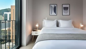 A hotel room with a large window, a bed with white linens, two framed artworks on the wall, and a bedside table with a lamp. - w Spectacular Loft w Balcony in El Nogal (Bogotá)