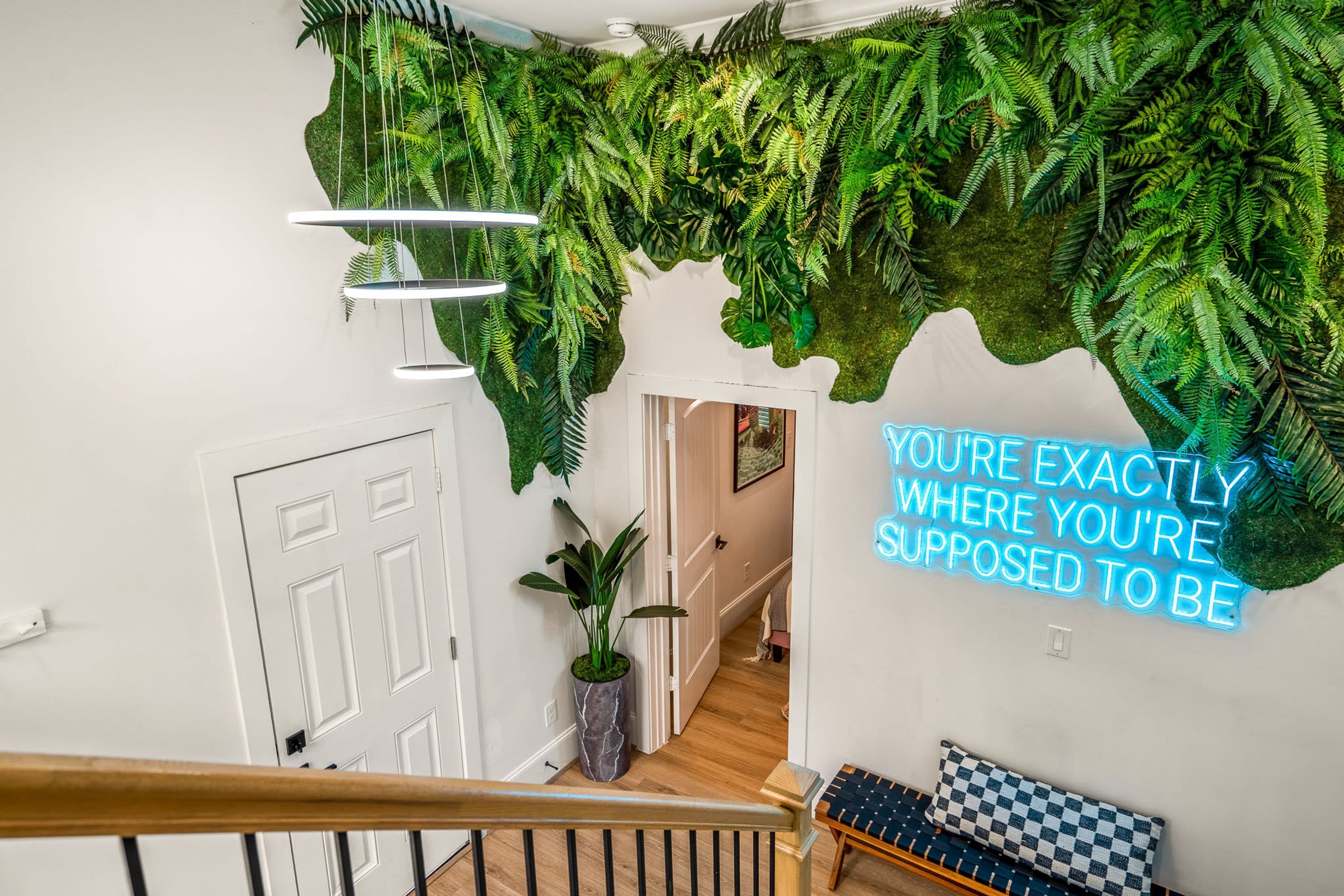 Un escalier avec une rampe en bois, une porte blanche et un panneau lumineux au néon sur le mur.