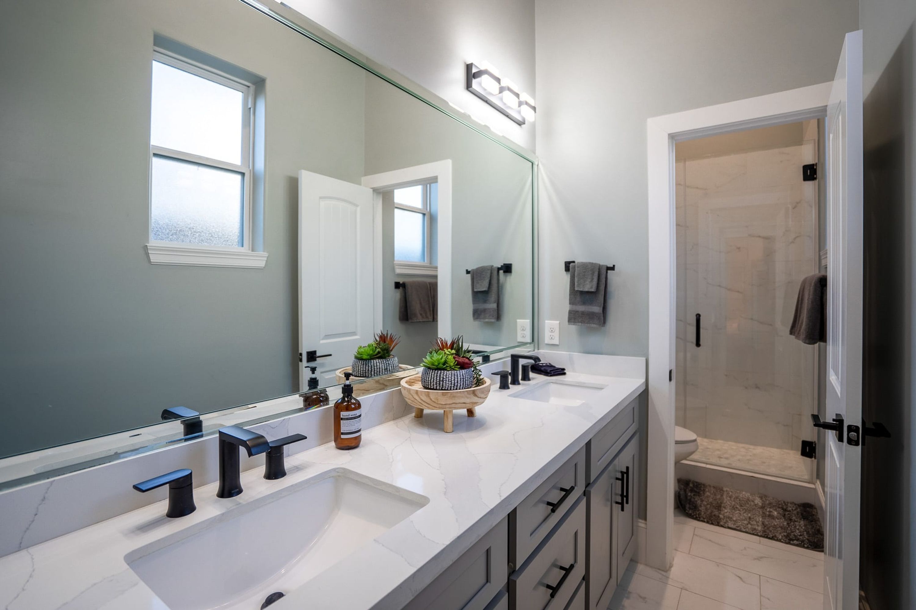 Une salle de bain moderne avec un grand miroir, deux lavabos et un espace douche.