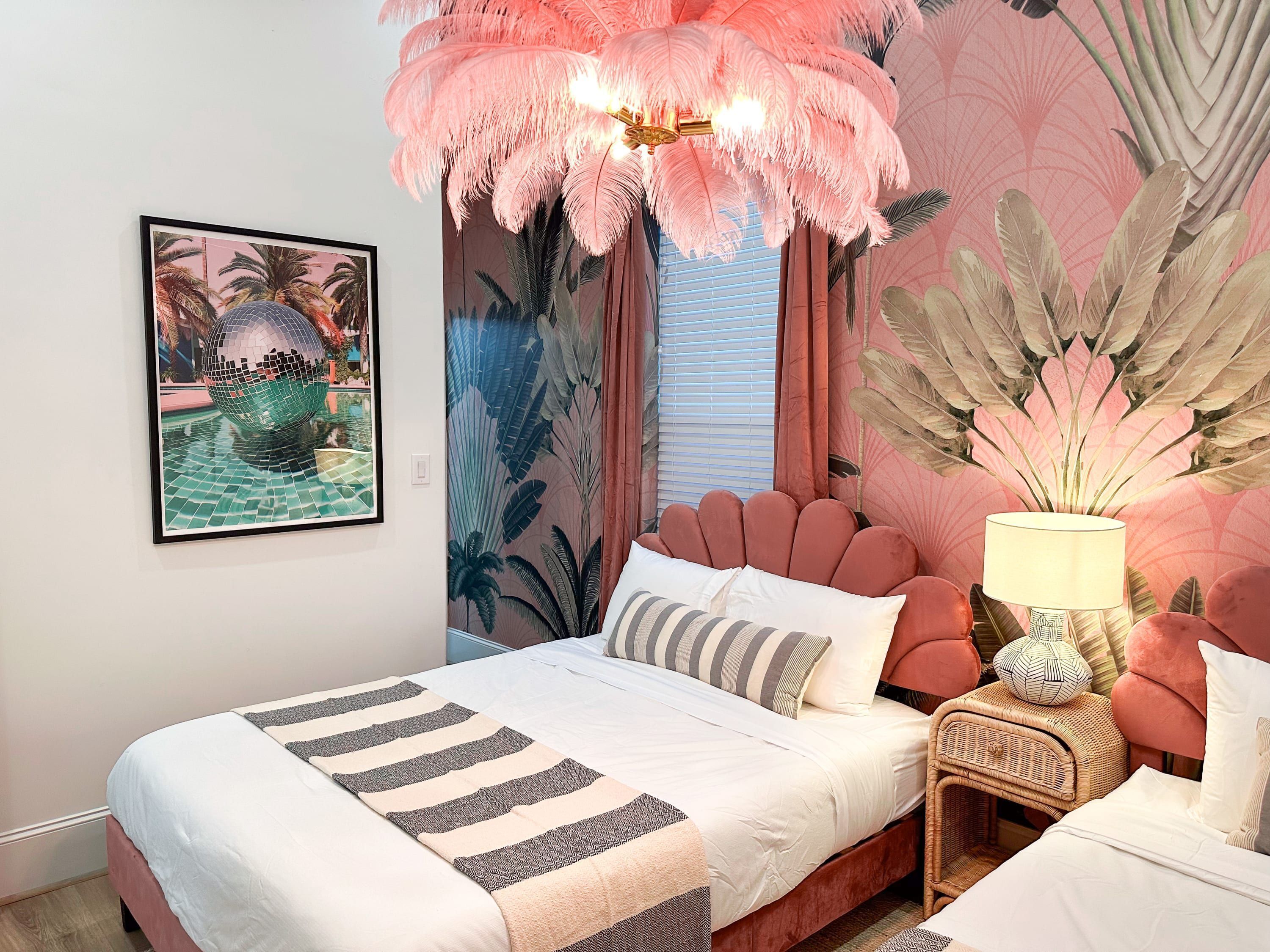 A bedroom with a bed, a nightstand, a lamp, and a wall with a tropical mural.