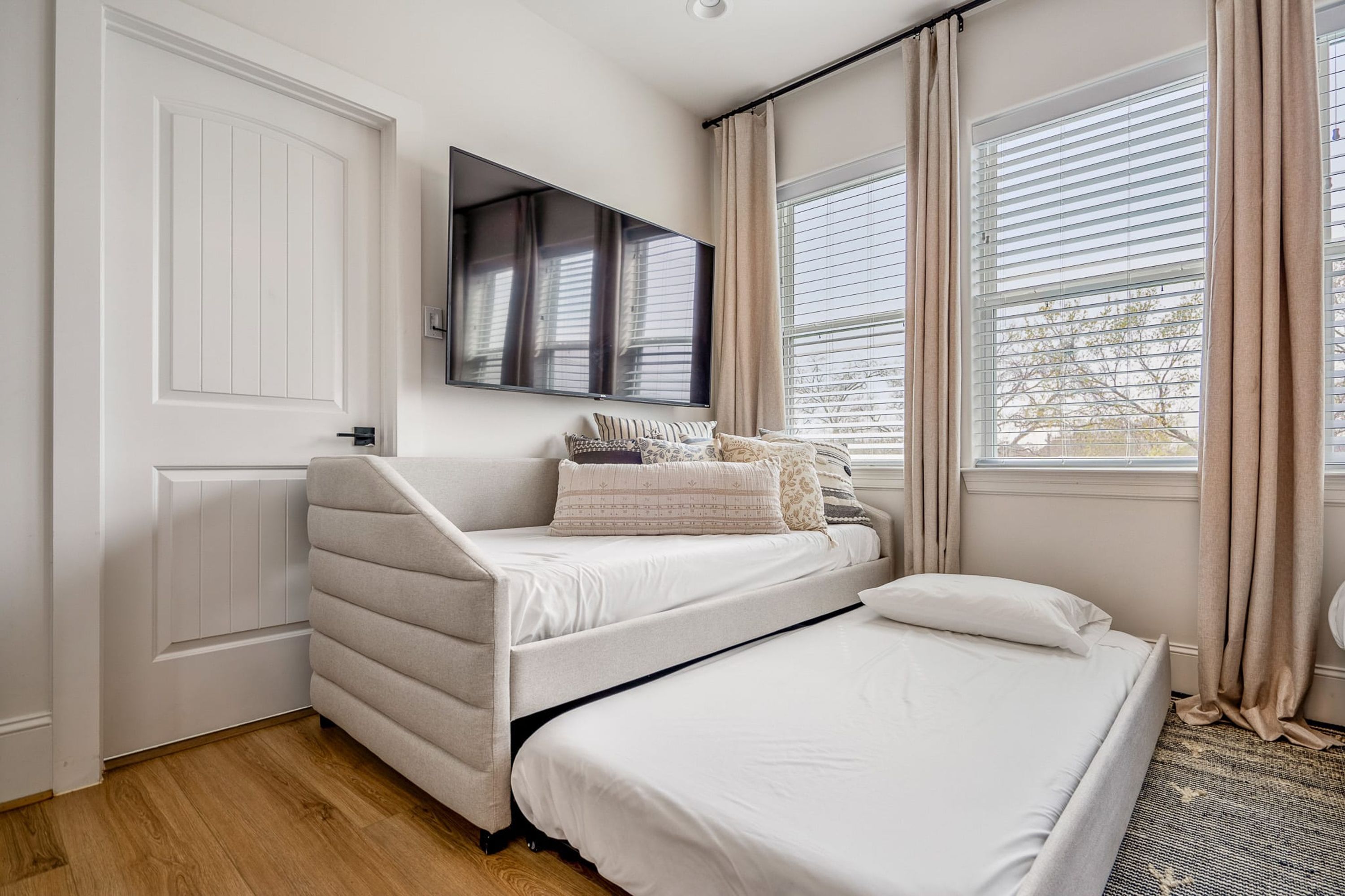 A bedroom with a bed, a sofa bed, a TV, and a window with curtains.