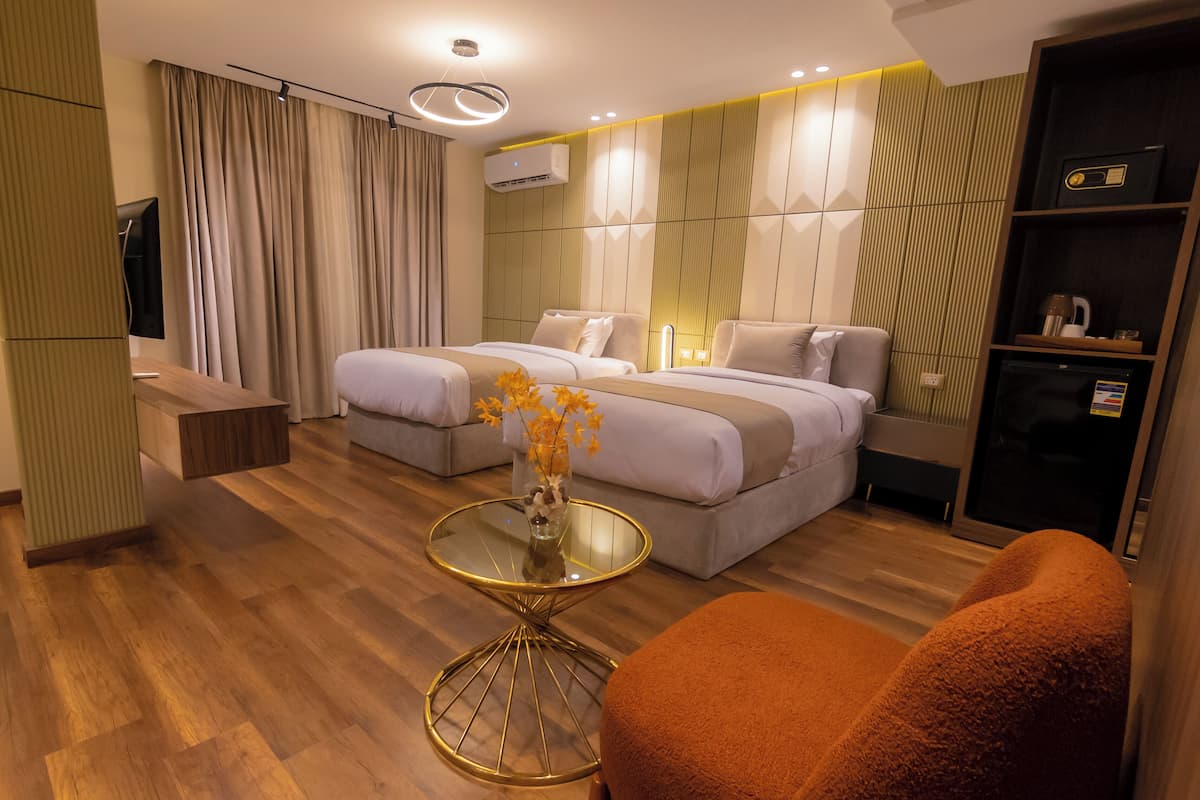 Moderni hotellihuone, jossa on kaksi sänkyä, lasipöytä, televisio ja vaatekaappi.