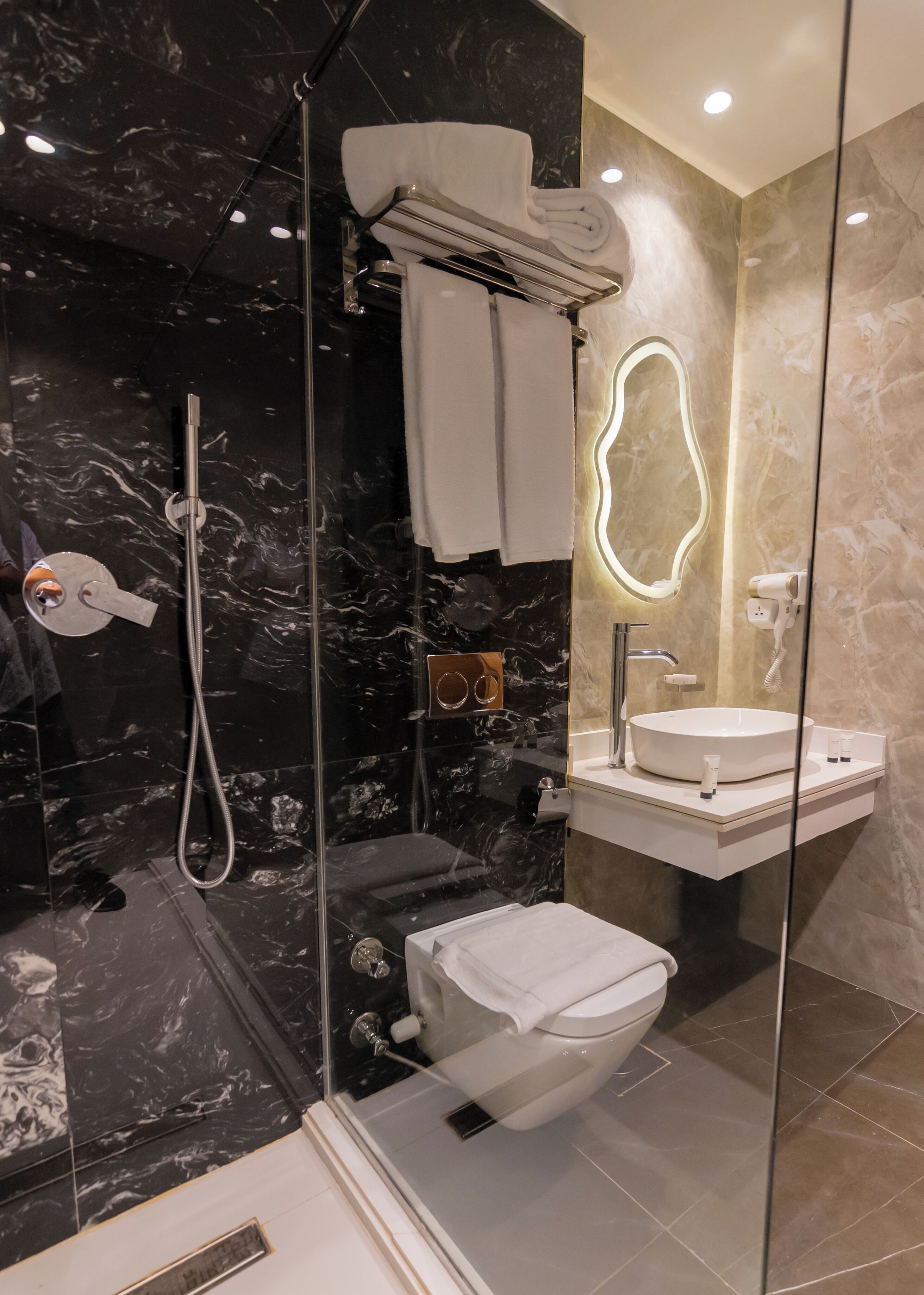 A modern bathroom with a glass-enclosed shower, a white toilet, a vanity with a mirror, and a towel rack.