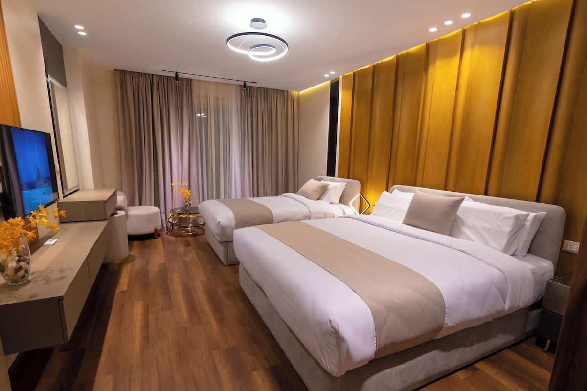 Moderni hotellihuone, jossa on kaksi sänkyä, työpöytä, jossa on televisio, ja suuri ikkuna, jossa on verhot.