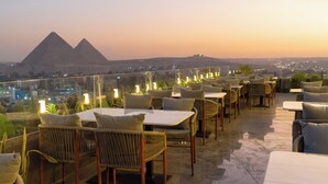 En tagterrasse med udendørs siddepladser og udsigt til pyramider.