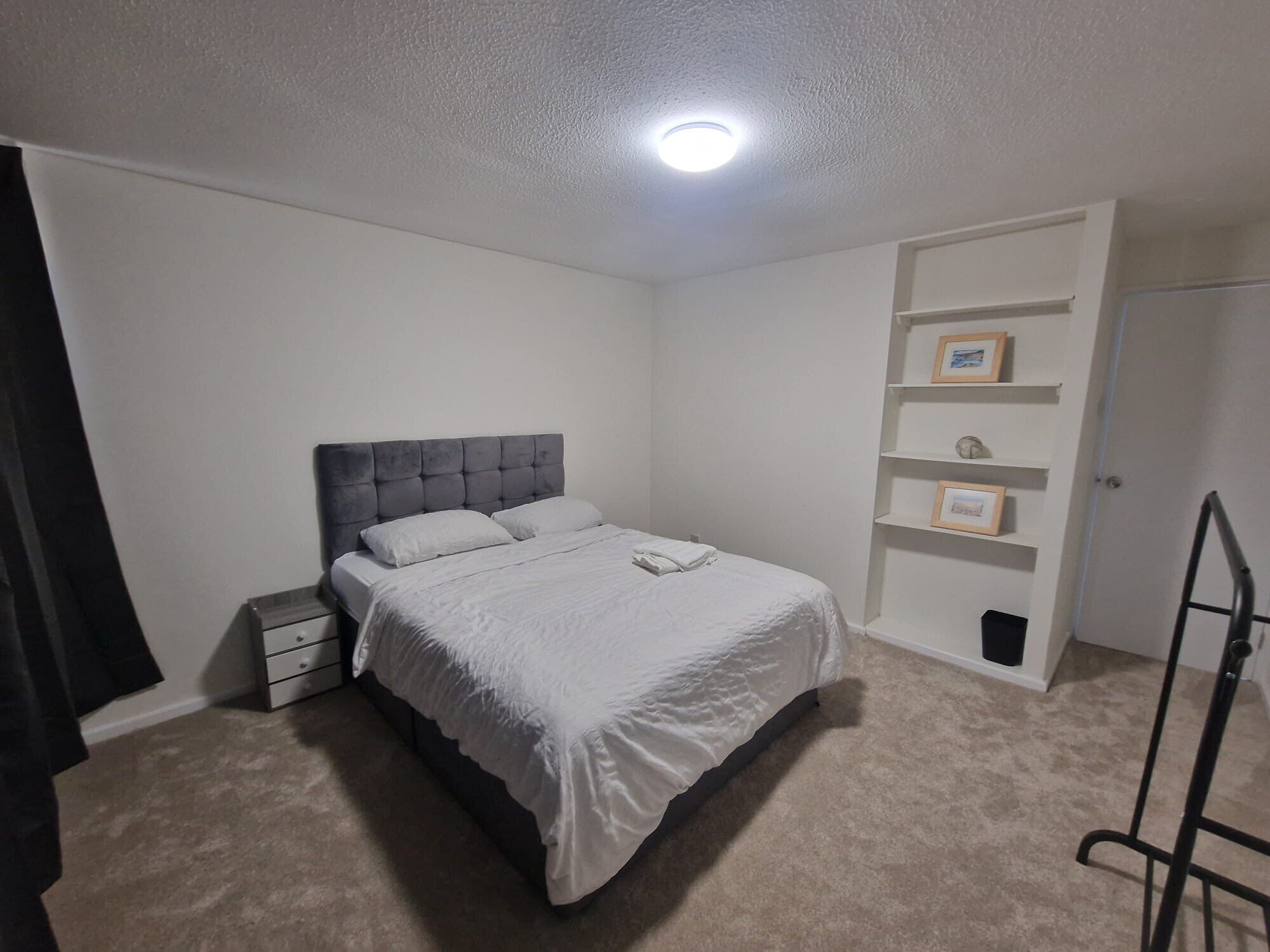 Une chambre à coucher comprenant un lit, une table de chevet, une armoire, une étagère avec des photos encadrées et une porte.