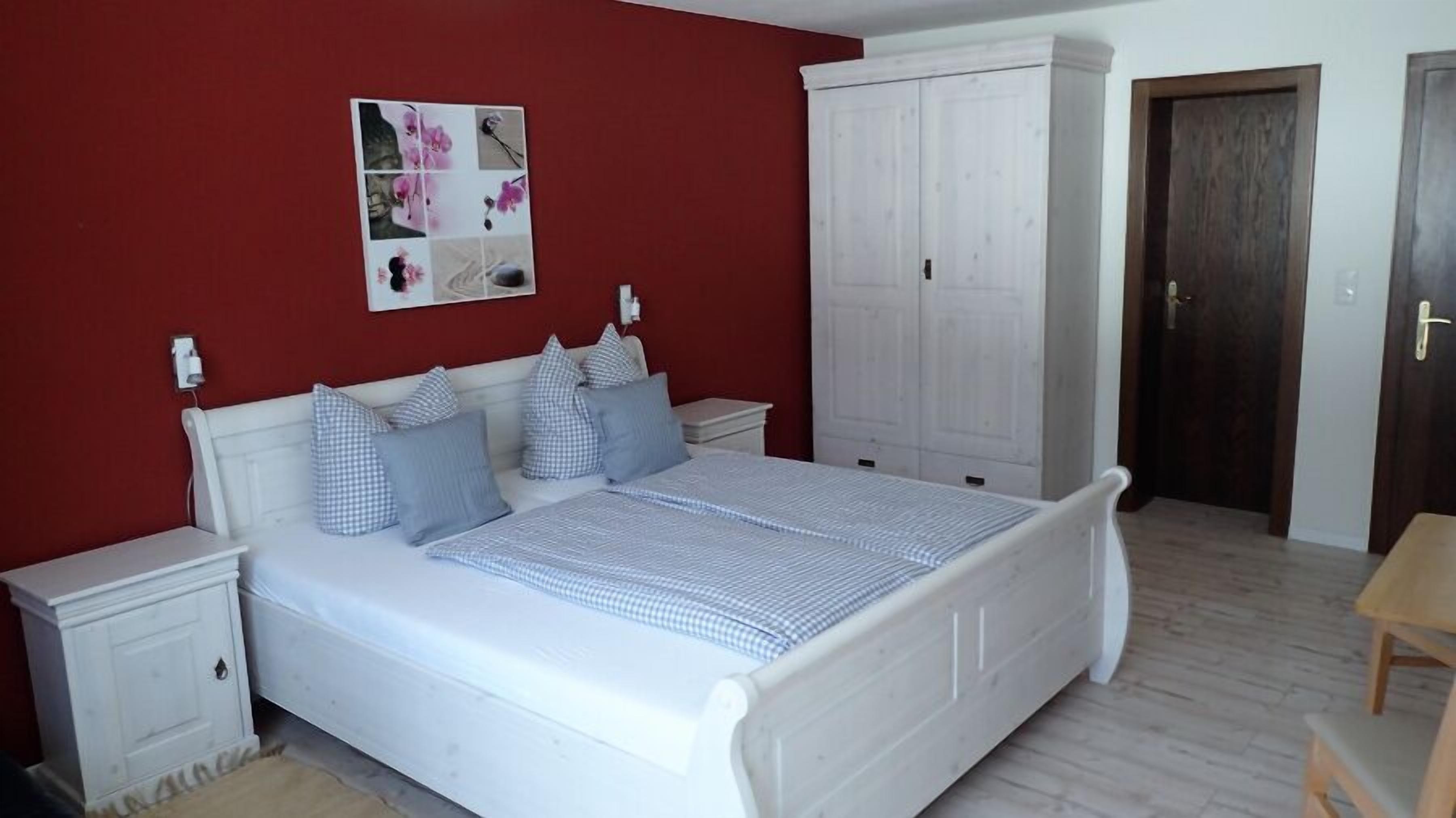 Un dormitorio con cama, mesitas de noche blancas, un armario y una pared roja.