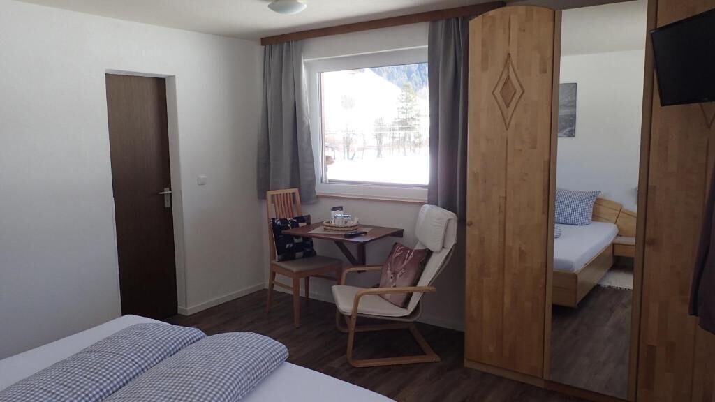 A hotel room with a bed, a desk with a chair, a TV, and a window with curtains.