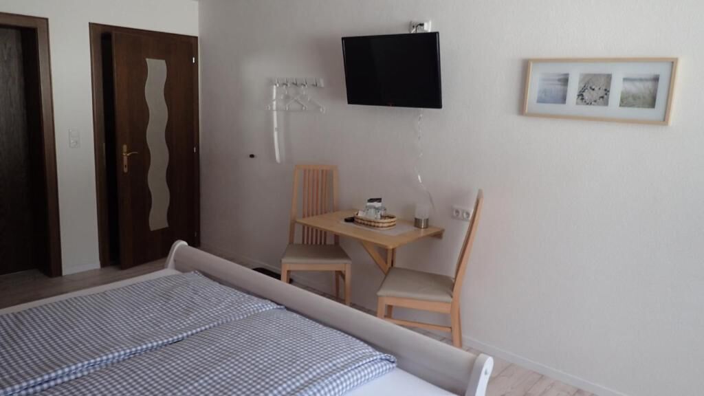Un dormitorio con cama, escritorio, dos sillas, televisor y un cuadro en la pared.