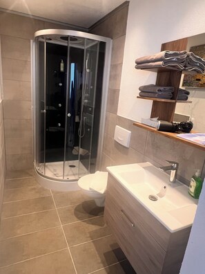 Un baño moderno con ducha envuelta en vidrio, un lavamanos blanco y un mueble de tocador de madera.