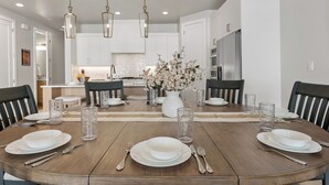 A dining area with a wooden table set for four, surrounded by chairs. There are hanging pendant lights above the table. - Desert Family Fun: Desert Color Lagoon + Beaches (St. George)