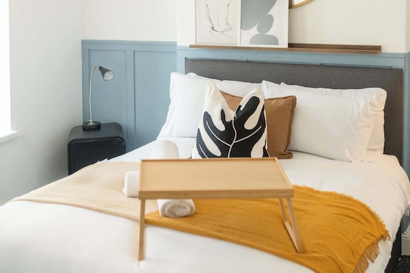 A neatly made bed with a wooden bedside table, a lamp, and a framed artwork above it.