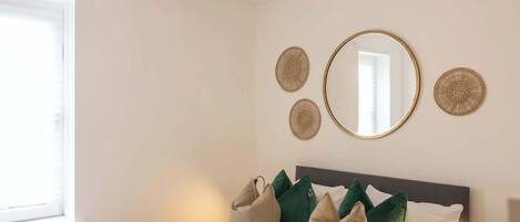 Un dormitorio con cama, almohadas, un espejo y adornos en la pared.