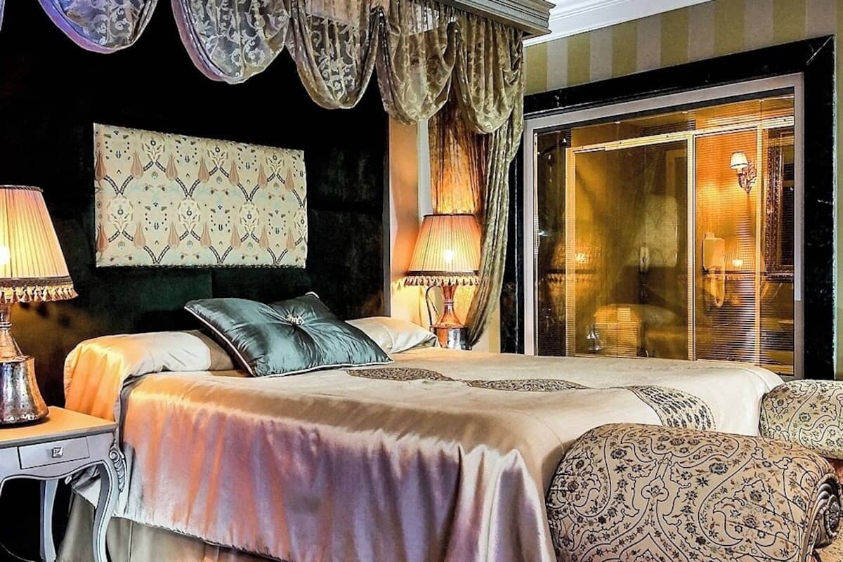 Ein Schlafzimmer mit einem großen Bett, zwei Nachttischlampen, einem gemusterten Kopfteil und Blick durch eine Glastür.