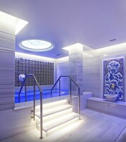 Un baño moderno con un jacuzzi iluminado en azul, un tragaluz circular y una pared decorada con azulejos.