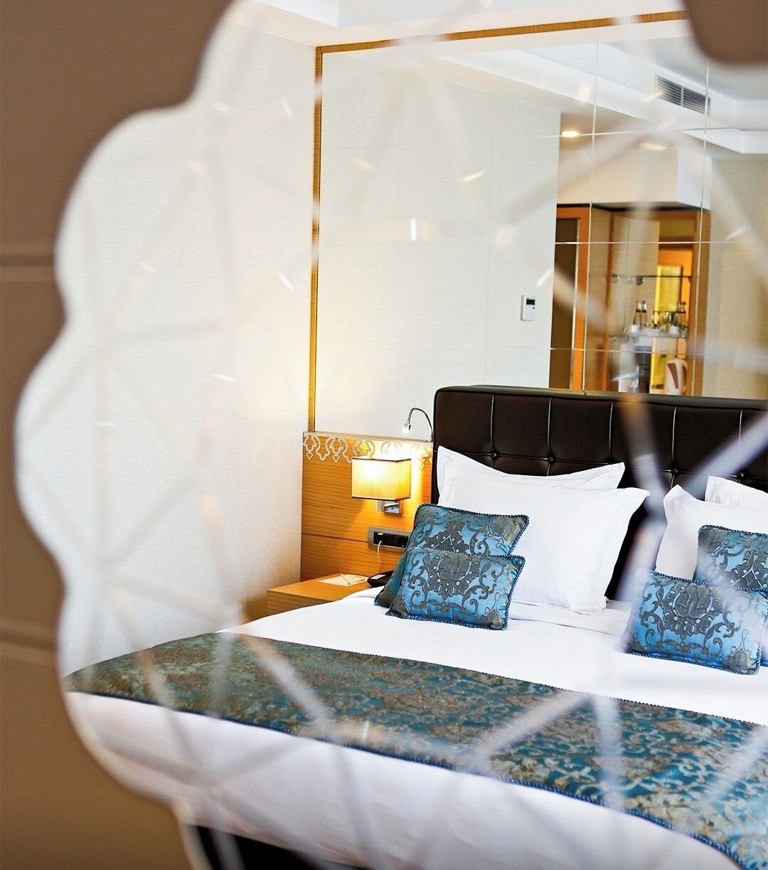 Quarto de hotel com cama, mesa de cabeceira, abajur e espelho.