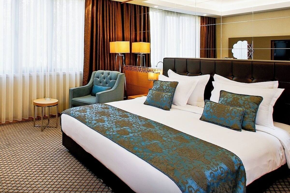Ein Hotelzimmer mit einem großen Bett, zwei Sesseln, einem kleinen Beistelltisch und einem großen Spiegel.