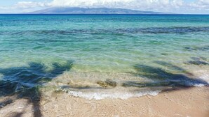 En strand med kristallklart turkost vatten, en sandstrand och ett berg i bakgrunden.
