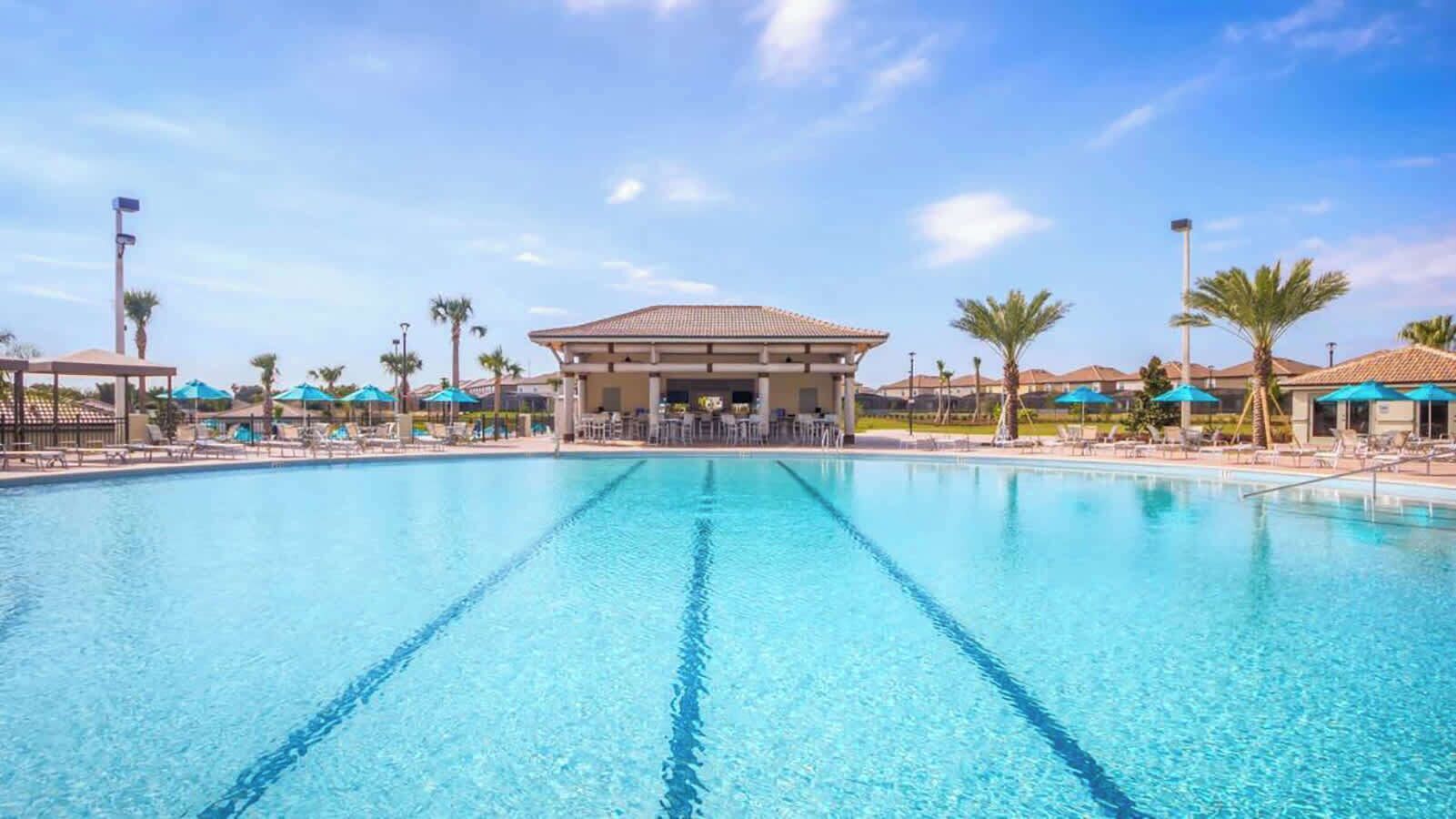 A large outdoor swimming pool with clear blue water, surrounded by lounge chairs and umbrellas.