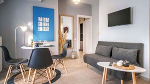 Een moderne woonkamer met een grijze bank, een ronde salontafel en een eethoek met een witte tafel en zwarte stoelen.