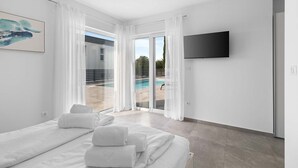Une chambre d’hôtel moderne avec un lit, des rideaux blancs, une télévision et une vue sur une piscine.