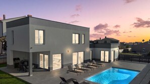 Une maison moderne à deux étages dotée d’une piscine, d’un espace salon extérieur et d’un coin barbecue.