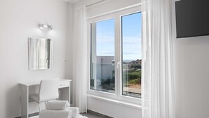 Une chambre d’hôtel moderne dotée d’une grande fenêtre, d’un bureau, d’une chaise et d’un lit avec des serviettes.