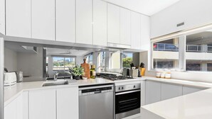 Une cuisine moderne avec des meubles blancs, un lave-vaisselle, un four et une fenêtre donnant sur la ville.