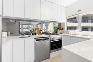 Una cocina moderna con armarios blancos, lavavajillas, horno y ventana con vista a la ciudad.