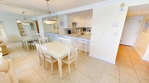 A modern kitchen with white cabinets, a granite countertop, and a dining area with a glass table and white chairs. - Beach House 602a 2 Bedroom Condo (Miramar Beach)