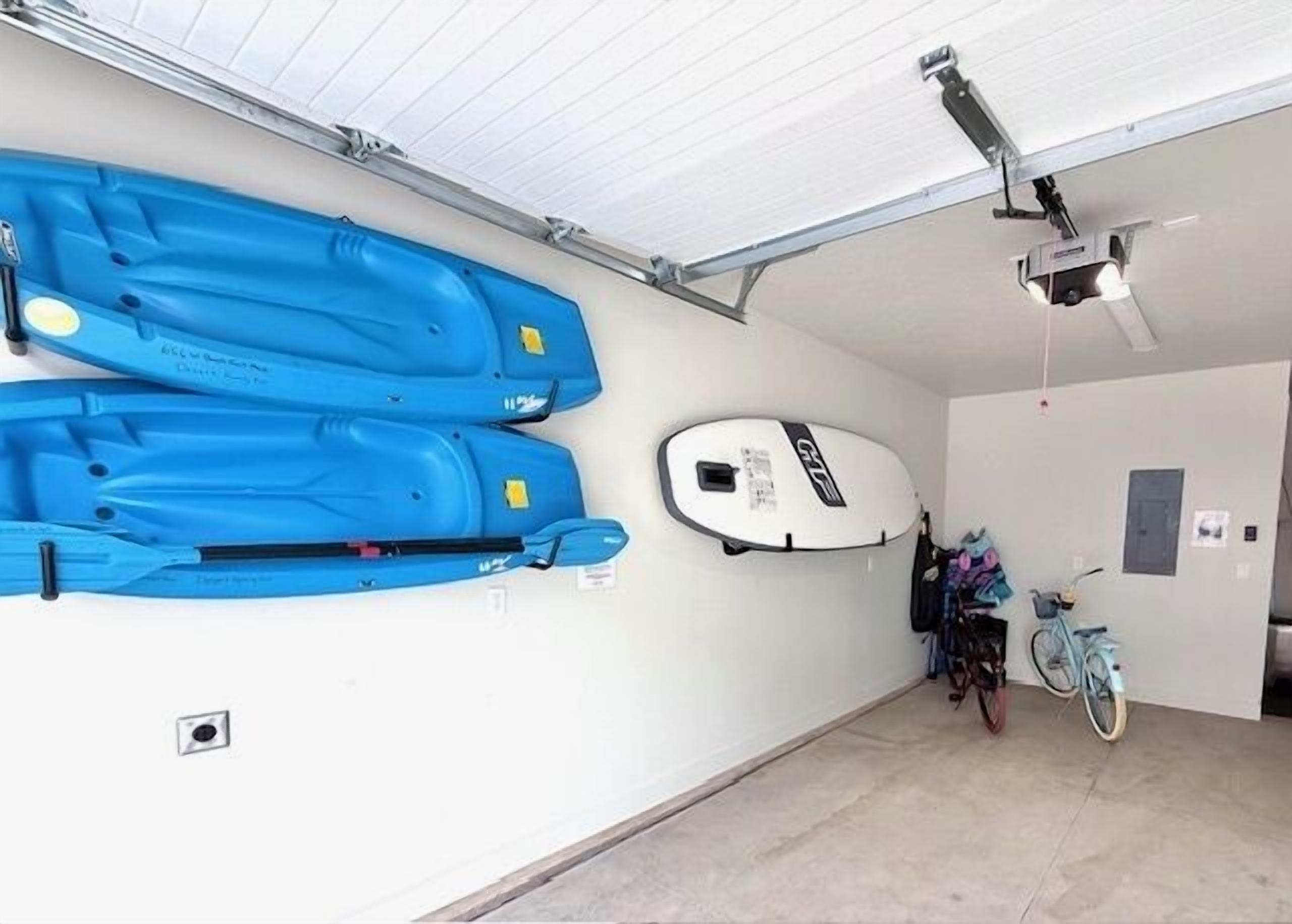 A garage with two blue kayaks, a white surfboard, and a bicycle.