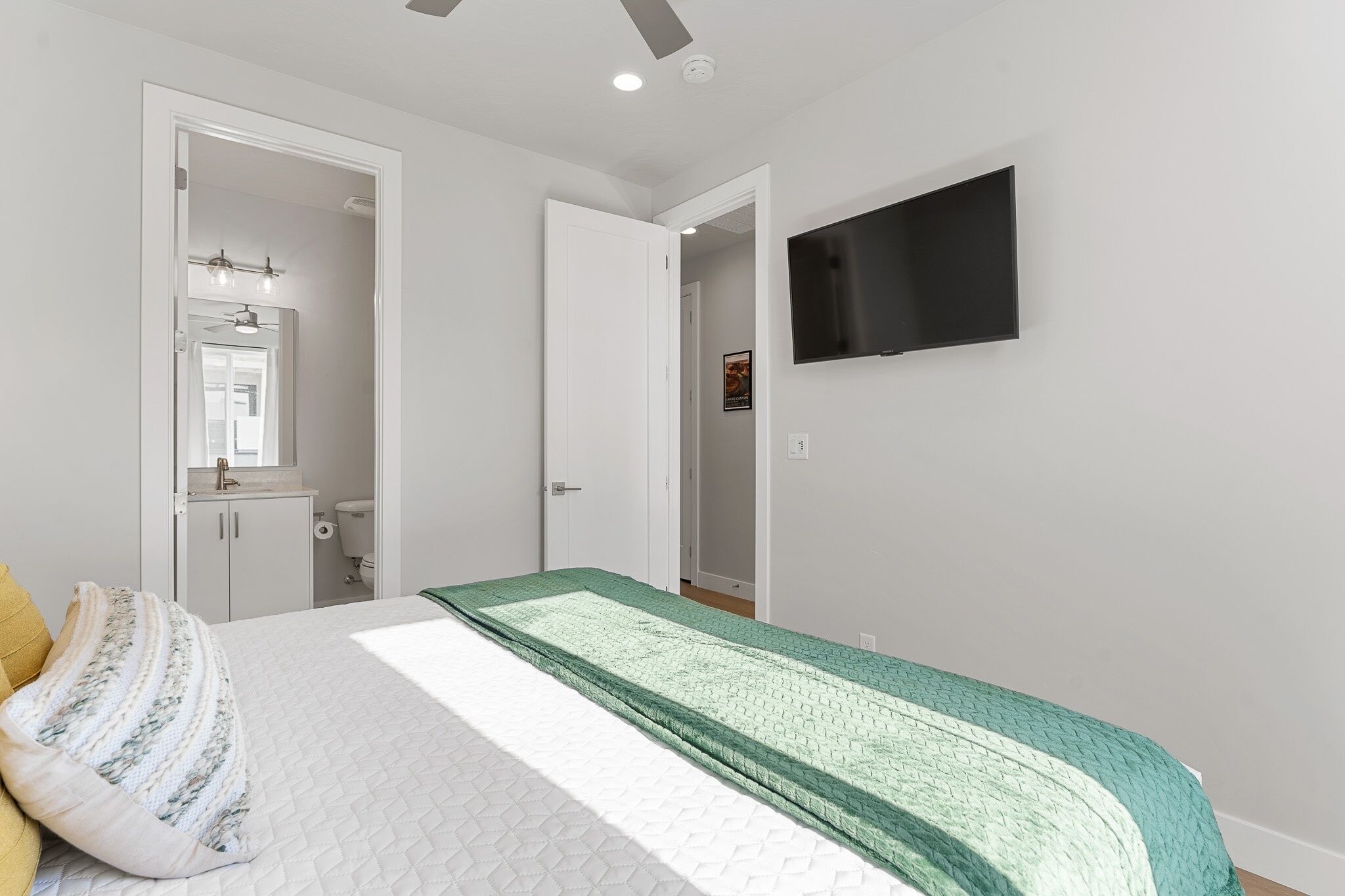 Un dormitorio con cama, televisor montado en la pared y baño a la vista a través de una puerta abierta.