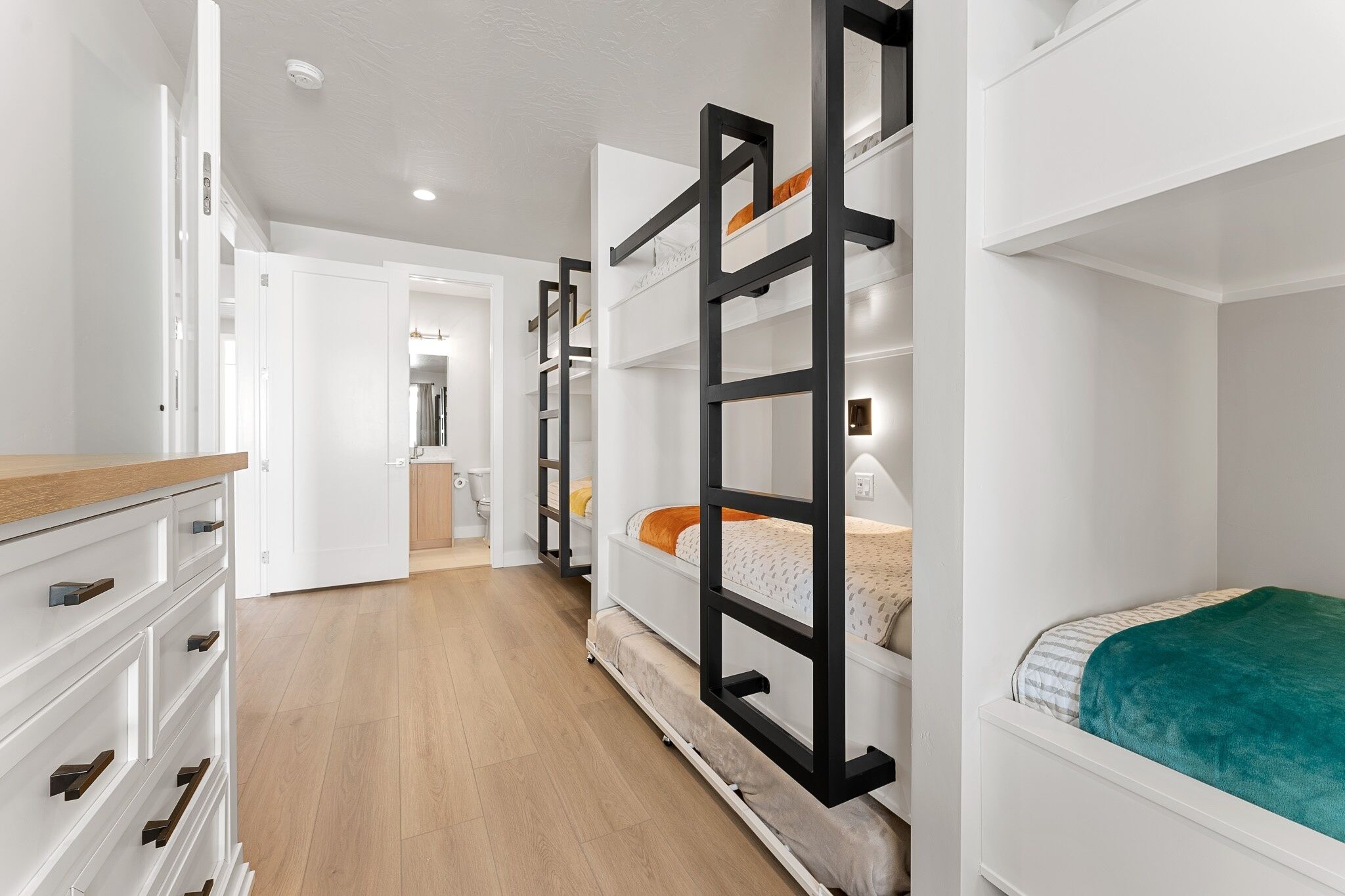 A bedroom with bunk beds, a wooden dresser, and a bathroom visible in the background.