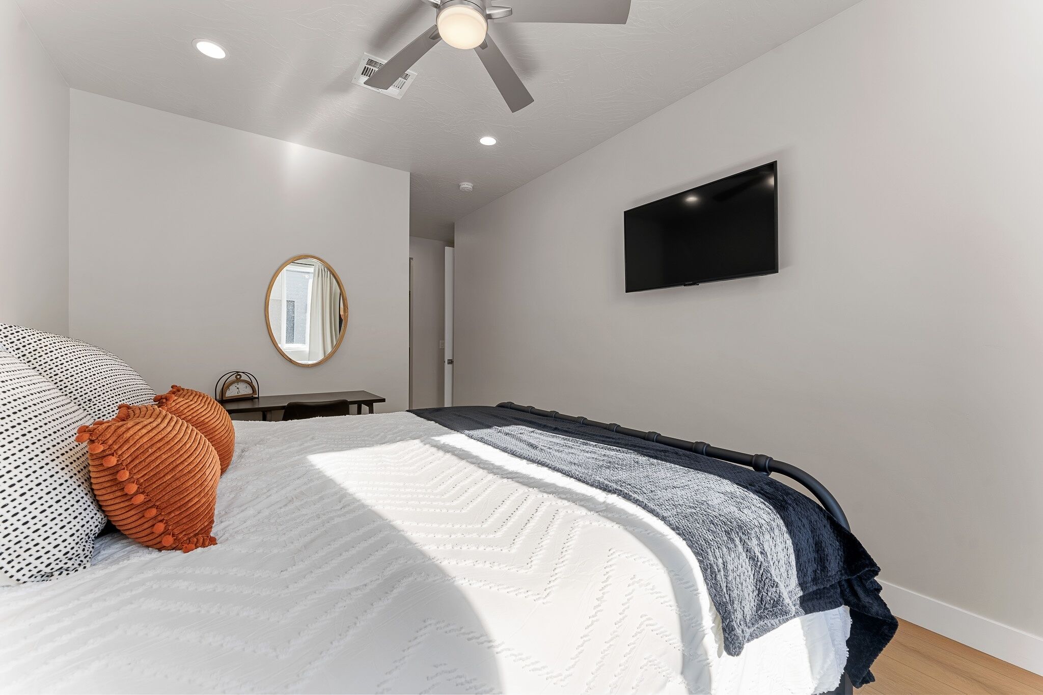 Een slaapkamer met een bed, een plafondventilator, een flatscreen televisie en een spiegel.