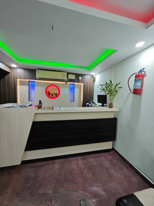 A reception desk with a modern design, including a wooden counter, a red circular decoration, and a fire extinguisher mounted on the wall. - NH Regency (Port Blair)