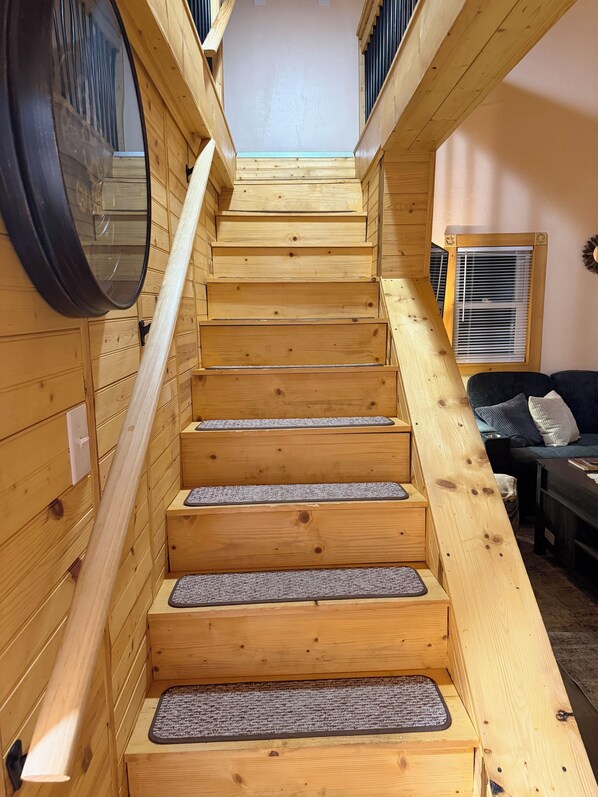 Un escalier en bois avec une rampe, des marches recouvertes de moquette et une fenêtre avec des stores.