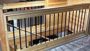Un balcón de madera con baranda de metal, una lámpara en el techo y vistas al interior.