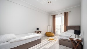 A modern hotel room with two single beds, a bedside table with a lamp, a small side table, a bean bag chair, and a view of the outdoors through large windows. - Apartamenty Sun & Snow Róża Wiatrów (Gizycko)