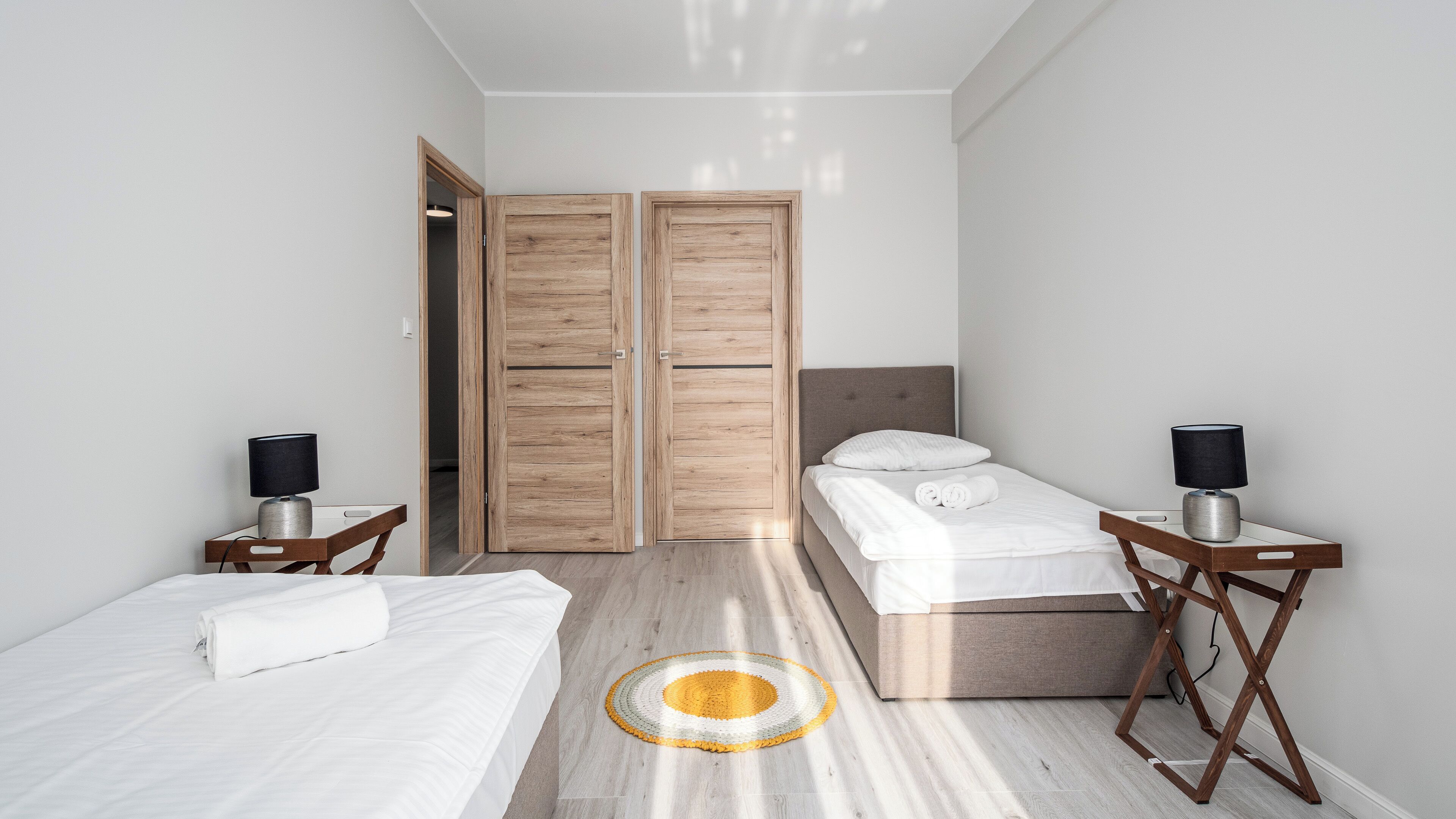 Een moderne hotelkamer met twee bedden, een grote houten garderobe en een rond vloerkleed.